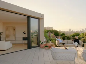 A modern residential patio with concrete flooring, steel railing, glass window, and upholstered seating.