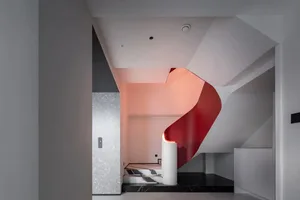Modern staircase with red metallic wall, white flooring, and black-and-white striped carpet.