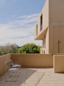 Concrete exterior of a minimalist building with a balcony and chairs.