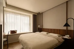 A minimalist bedroom featuring a bed covered with a cotton blanket and wooden paneling against a beige wall, natural light st