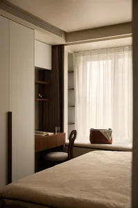 A minimalist bedroom with a bed, a chair, a desk, and a window with sheer curtains.