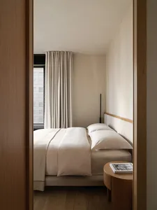 A minimalist bedroom featuring a comfortable bed with soft textiles and wooden accents.