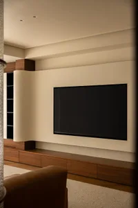 A minimalist living room with a modern, sleek TV mounted on the wall, wooden cabinets, and a comfortable leather chair.