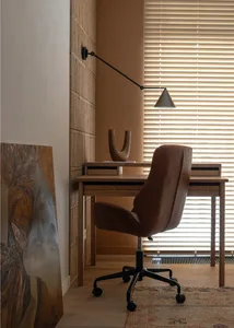 A minimalist workspace featuring a wooden desk, a brown leather chair, and a textured rug on a wooden floor.