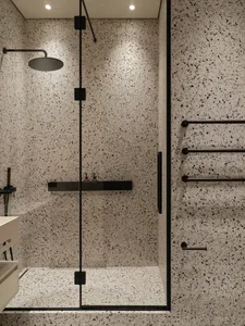 A modern bathroom featuring white terrazzo flooring and walls with black speckles, and minimal black fixtures