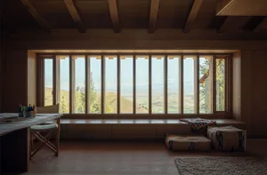 A modern interior with a large window showcasing a view of the hills and mountains, featuring a wooden bench, a table with dr