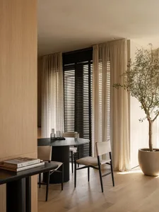 A modern interior design featuring wooden elements and lighting. The space includes a round table, chairs, and a tall plant.