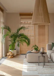 A modern, minimalist living room with neutral-toned furniture and decor, featuring a large potted palm plant and wooden floor