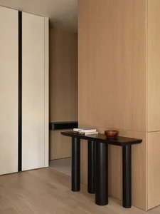 Modern indoor console table with wood surface and black cylindrical legs, positioned in a minimalist room with wooden walls a