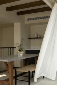 A minimalist industrial-style kitchen with exposed wood beams, concrete countertops, and a plant on the table.