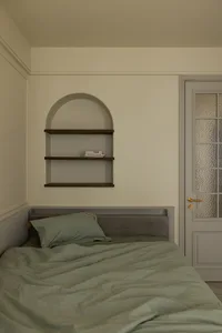 A minimalist bedroom with a bed, pillows, and a shelf.