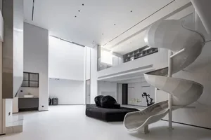 A minimalist, all-white residential interior featuring a spiral slide and black bean bag chairs.