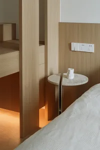 Bedroom with modern design and wooden furniture, including a round side table with a vase.