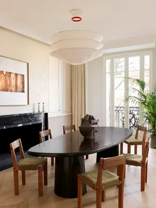 A modern dining room featuring an oval marble table with wooden chairs and fabric cushions, set in front of a marble fireplac