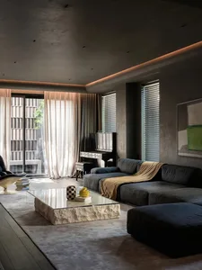 A modern living room featuring a large blue sofa with a golden throw, a black piano, and a glass-top coffee table on a grey r