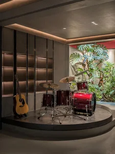 A modern music studio featuring a red drumkit, guitar, and tropical plants in the background.