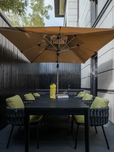 Outdoor dining area with modern, black, composite material furniture, green cushions, and a large beige umbrella.