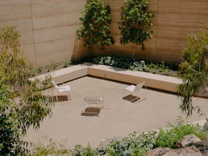A minimalist outdoor patio with a concrete floor, white chairs, and greenery.