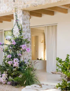 A residential entrance featuring a stone wall adorned with purple flowers, wooden beams, and a white curtain.