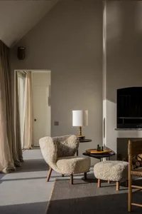 A cozy living room with a sheepskin chair and ottoman, a side table with a lamp, and a fireplace.