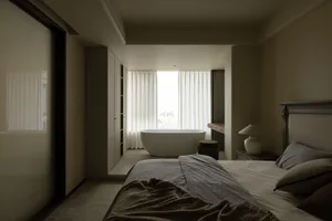 A minimalist bedroom features a concrete floor and a freestanding bathtub with sheer curtains.