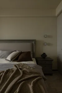 A minimalist bedroom featuring a bed with a knitted blanket, a headboard, and a bedside table with decorative items.