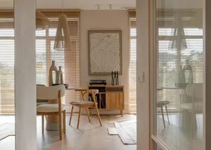A minimalist dining room with wooden furniture and light-colored blinds.