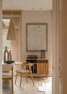 A minimalist living room featuring wooden furniture, a pendant light, and abstract wall art.