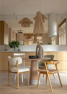 Modern dining room featuring a round wooden table with woven-straw pendant lights, fabric chairs, and concrete countertops.