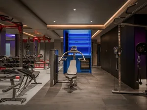 A modern home gym featuring black and blue lighting, with various exercise equipment including benches, bars, and weights.