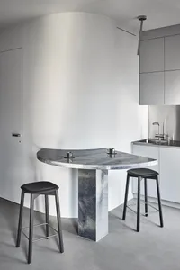 A modern kitchen with a marble island and countertop, featuring minimalist design and sleek black stools.
