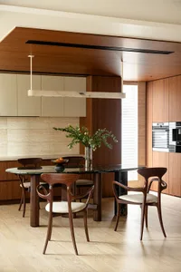 A modern kitchen with an oval dining table, wooden chairs with white upholstery, and a marble countertop. Features include wo