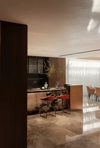 Modern living room featuring a sleek bar counter with marble top and two red stools, set against a warm, minimalist interior 