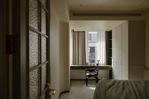 A modern minimalist bedroom featuring a window with curtains, a green desk, black chair, and a bed with a green blanket.