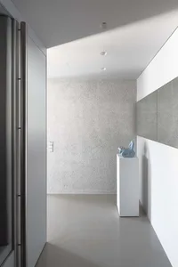 Modern minimalist entryway with textured concrete walls and a sculptural blue object displayed on a pedestal.