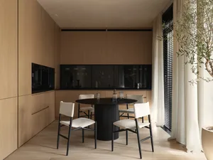 A modern residential kitchen featuring wooden cabinets, a black dining table, and white upholstered chairs.