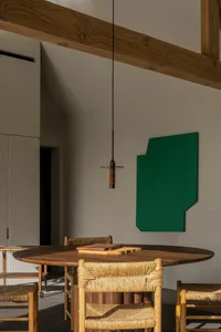 A modern kitchen interior with a round wooden table and chairs, featuring a green abstract wall art and exposed wooden beams.