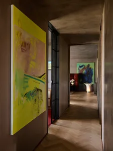 A hallway with wooden flooring and concrete walls adorned with abstract art hanging on the walls.