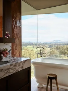 A luxurious bathroom featuring marble and concrete finishes, with a view overlooking trees and hills.