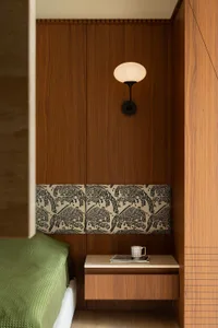 A minimalist bedroom features a floating wooden nightstand with a lamp and a cup and magazine on top.