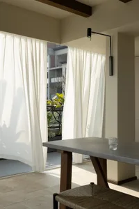 A minimalist interior space featuring textured cloth curtains, a concrete table, and a woven chair.