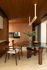 A minimalist kitchen with wood cabinets, marble countertops, and a round dining table with white chairs.
