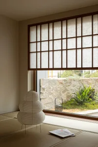 A minimalist living room with a paper-laminate floor, paper lantern, and stone wall with plants and a paper blind.