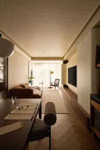 A minimalist living room featuring wooden furniture, a leather sofa, and a flat-screen TV mounted on a wall with built-in sto