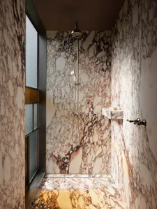 Modern minimalist bathroom with marble walls, shower, and a window.