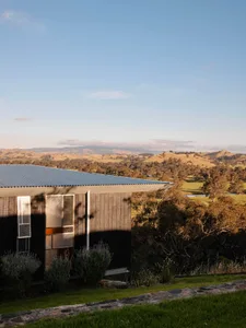 A modern house with a wooden exterior and metal roof in a rural landscape.