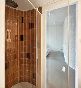 A modern bathroom featuring curved walls made of brown tiles, with a sleek glass enclosure.