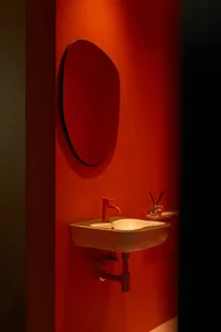 Modern bathroom with a red wall, ceramic sink, and round mirror.