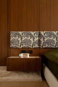 A modern bedroom with wooden accents, featuring a headboard with animal patterns, a nightstand, and a lamp with an 'X' design
