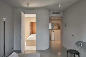 A modern bedroom with a concrete wall, minimalist design, and a bed with white bedding.
